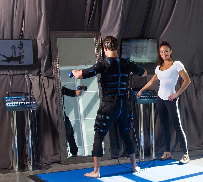 Daniel Nyiri exercises while wearing the full-body EMS while 2 X Miss Olympia Erin Stern monitors the E-1250 control panel.