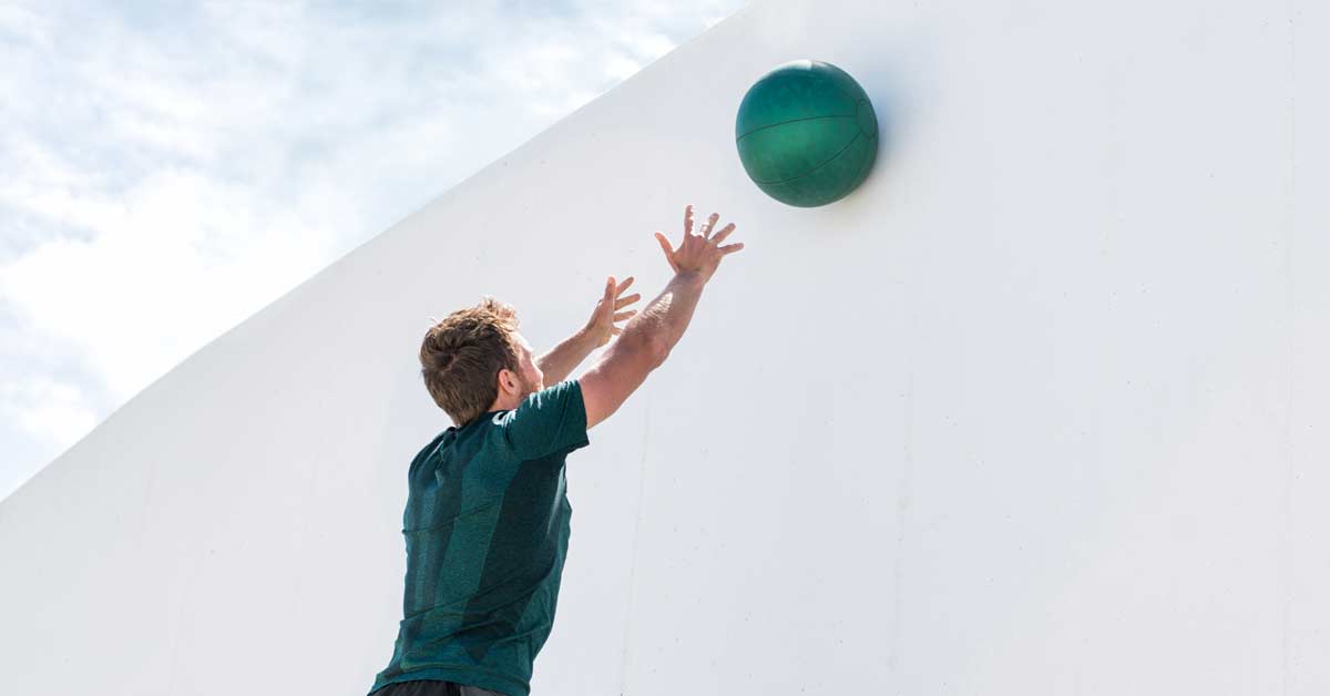 man in green shirt doing overhead medicine ball throws