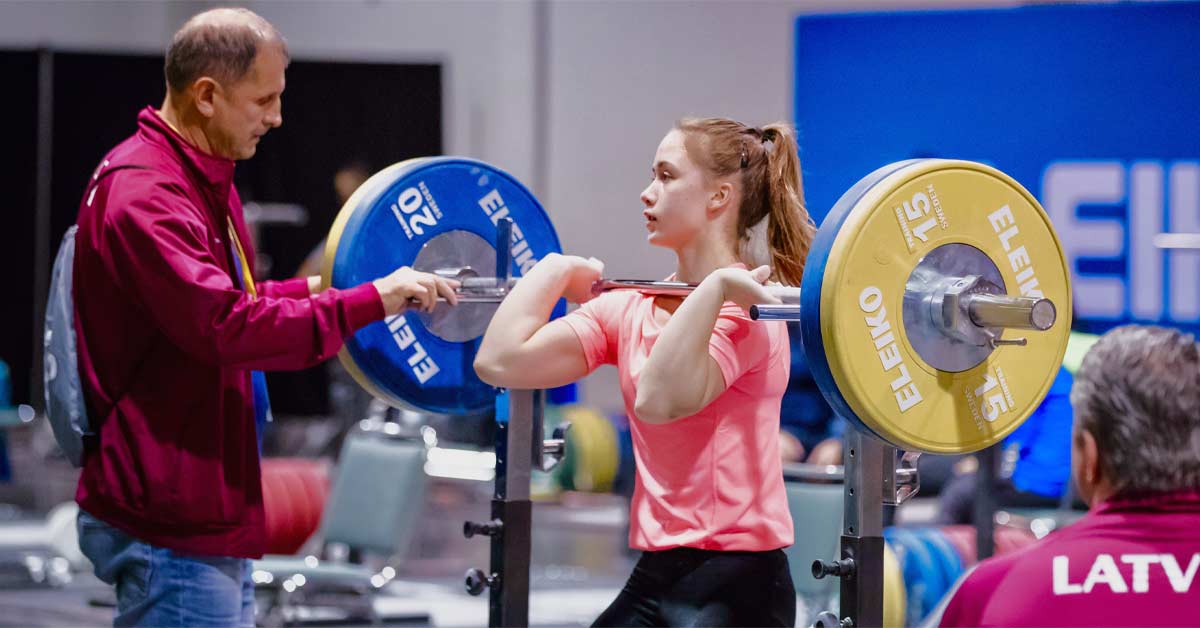 Personal Trainer Showing Young Woman How To Train Barbell Squats