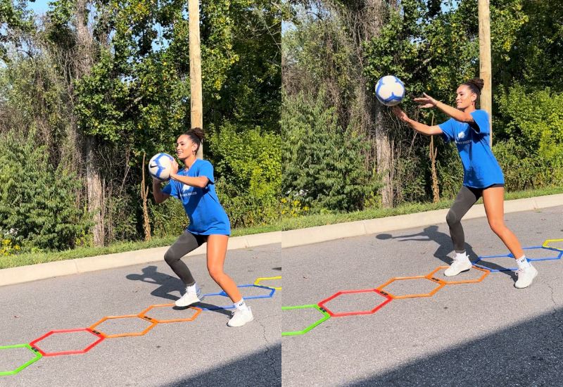 A woman in athletic wear stands outdoors on a paved surface, holding and then tossing a blue-and-white soccer ball while stepping through colorful hexagons arranged on the ground. Trees and greenery are in the background.