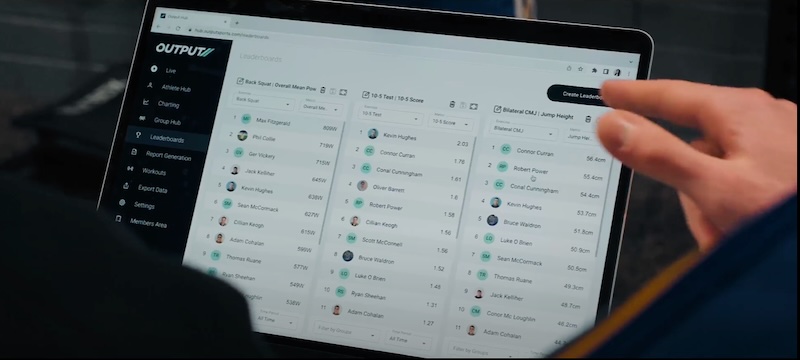 A person uses a laptop displaying a sports fantasy dashboard with player lists, stats, and team management options on the screen. The interface shows various selectable tabs and user information.