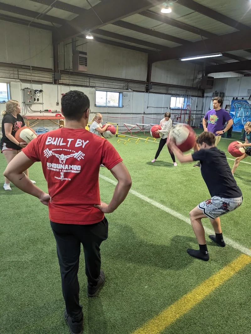 Athletes at training facility use medball pulldown throws to train in a low stress manner.