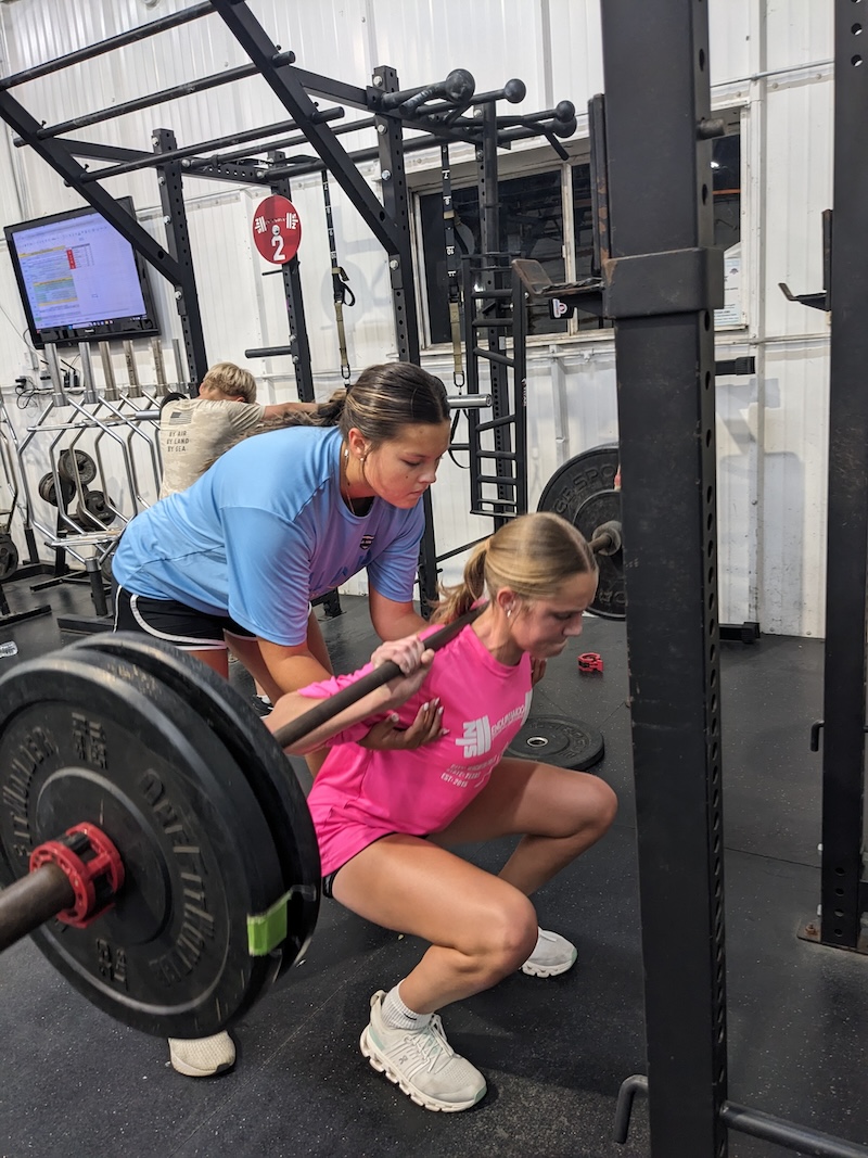 Female athlete executes squat lift in a power rack.