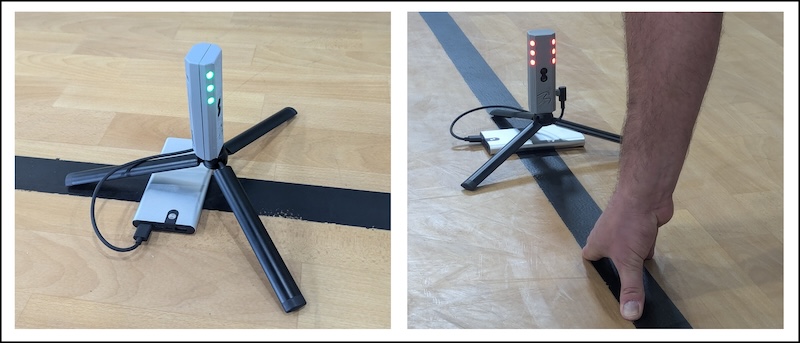A small tripod-mounted electronic device with red and green lights is on a wooden floor. In the second image, a person is adjusting or using the device next to a black line on the floor.