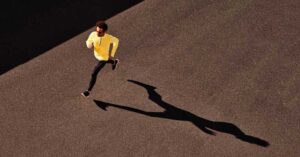 A person in a yellow top and black pants is running on a wide