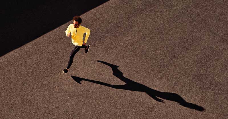 A person in a yellow top and black pants is running on a wide