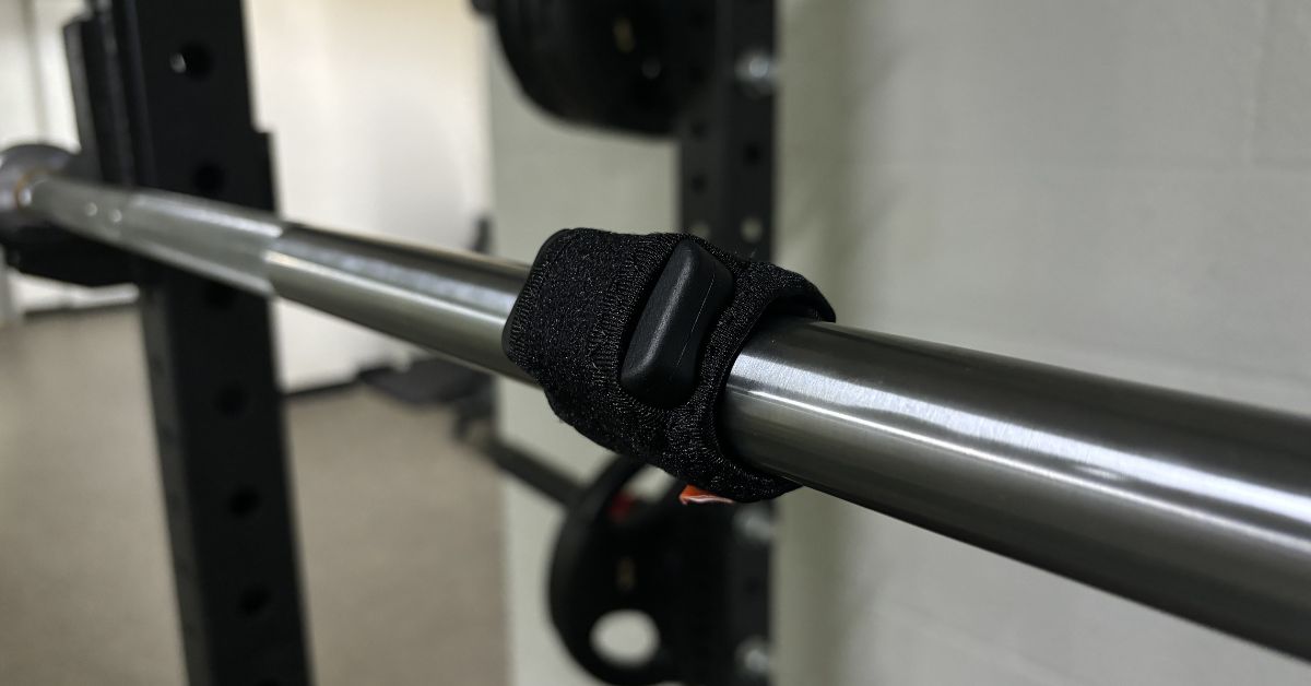 The Enode Pro sensor inside its barbell sleeve attached to a barbell.|An athlete using the Enode sensor on the barbell during squats.|An open black zippered case with foam cutouts and a mesh pocket is shown. Below are a black wristband with an orange and white logo