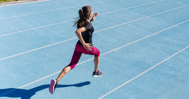 Female Athlete Running Track|A girls soccer team in blue uniforms is warming up on a field. They are practicing stretches in bright outdoor lighting
