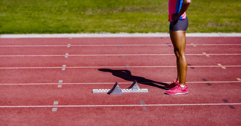 Female Sprinter Standing Behind Starting Block|Football Punt Return|Alabama National Football Championship|All State Relays|A man in a dark athletic shirt stands outdoors with his hand near his face