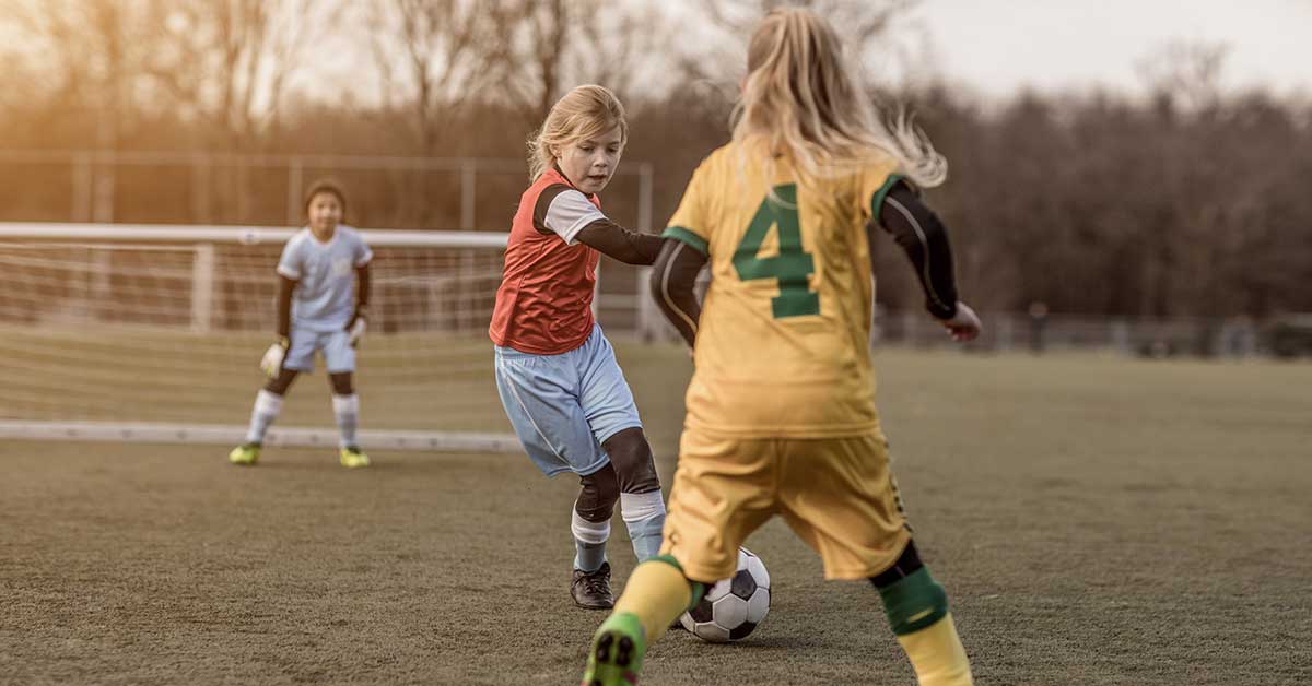 Girls Playing Soccer|Play 1 Play 2|Core Activity|A tactical diagram on a soccer field illustrating the 3v2 Through the Gates game. It includes player movements
