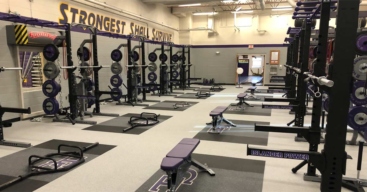 Grand Island|Branded Plates|Islander Power|The image shows a gym area with exercise equipment. On the left is a cable machine with a purple seat and handles. On the right