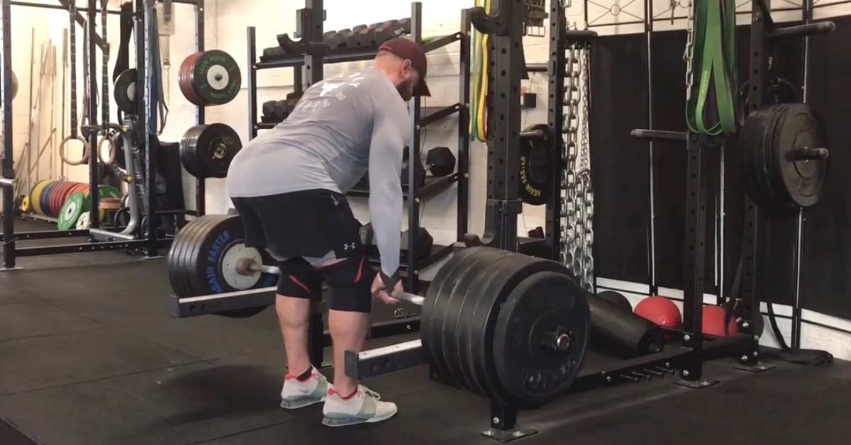 Header RDL Wayland|Wayland RDL|Unlocking knees|A person in a gym is performing a deadlift with a barbell. They are wearing a blue tank top
