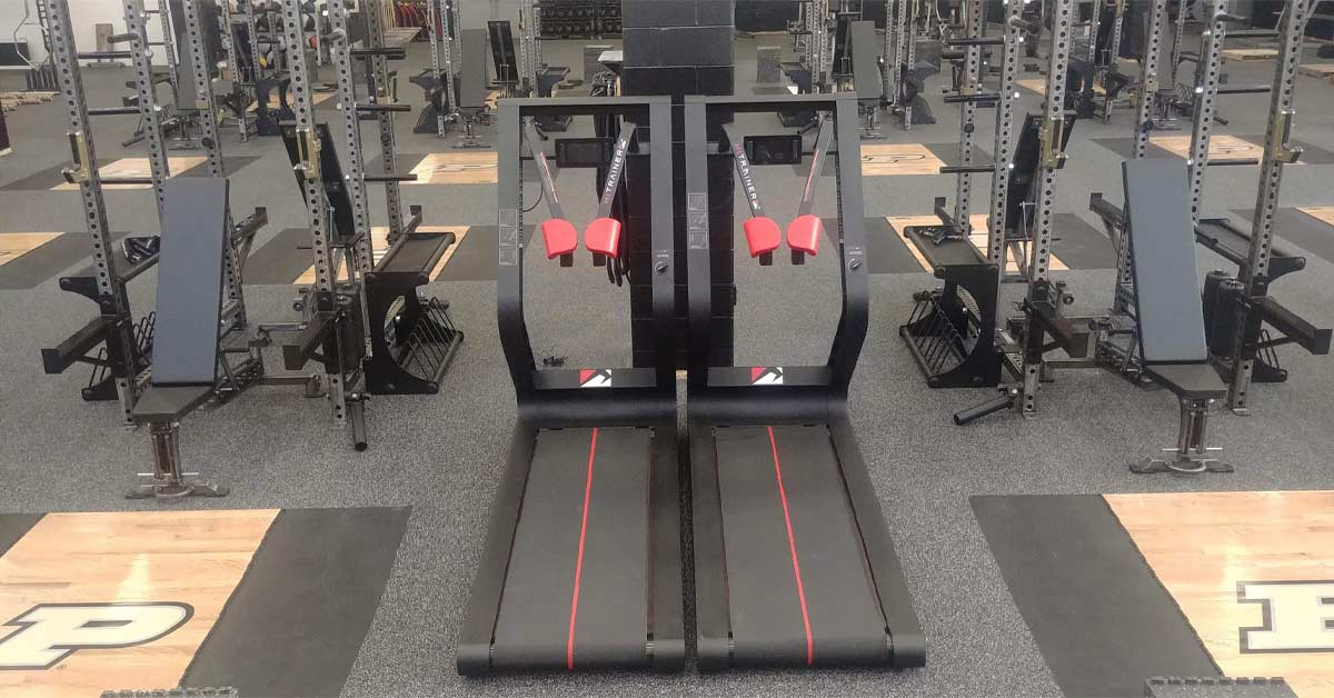 HiTrainer Gym|A man is running on a treadmill against a blue wall. He is wearing a navy blue shirt and shorts with white stripes
