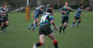 Rugby Specialization|A group of young men in black and yellow sports jerseys gather around a table with snacks. One person humorously wears a cardboard box on their head. The room has trophy plaques on the walls.|Paralympic Athlete