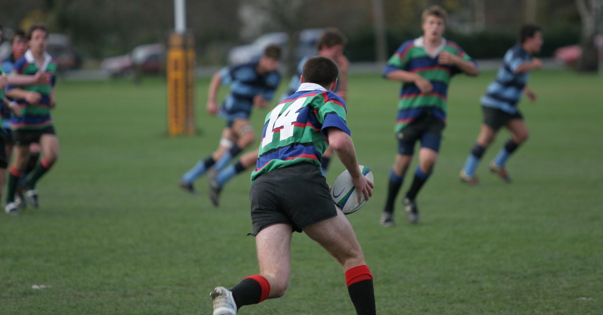 Rugby Specialization|A group of young men in black and yellow sports jerseys gather around a table with snacks. One person humorously wears a cardboard box on their head. The room has trophy plaques on the walls.|Paralympic Athlete
