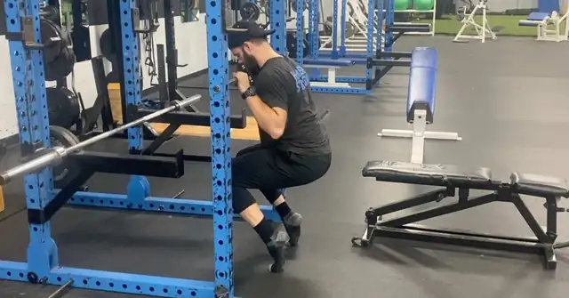 A man in gym attire performs a squat inside a blue power rack