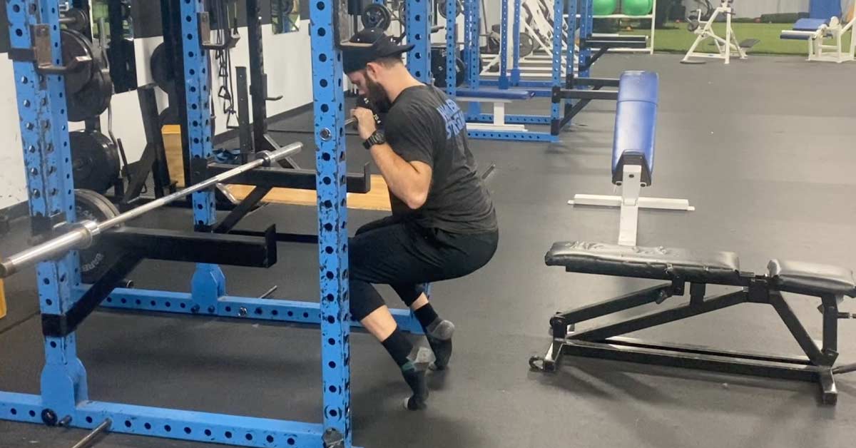 A man in gym attire performs a squat inside a blue power rack
