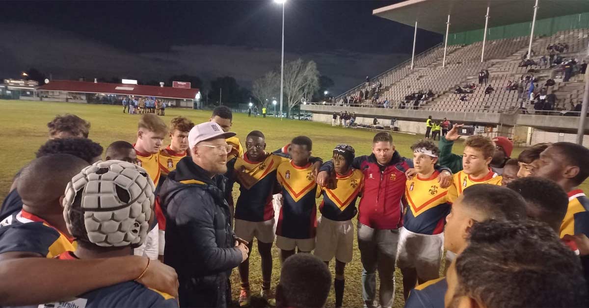 Murray Ingram Connect|A rugby team in bright red jerseys stands in a group huddle on a grassy field. They have their arms around each other