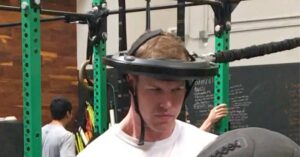 Iron Neck Athlete|Iron Neck Training|Concussion|Iron Neck System|A person wearing a helmet connected to a machine looks upward. The helmet is attached to a cable