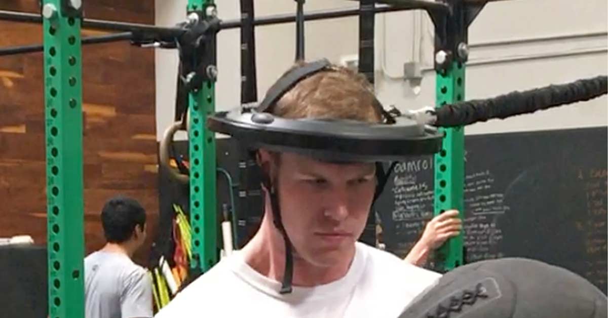 Iron Neck Athlete|Iron Neck Training|Concussion|Iron Neck System|A person wearing a helmet connected to a machine looks upward. The helmet is attached to a cable