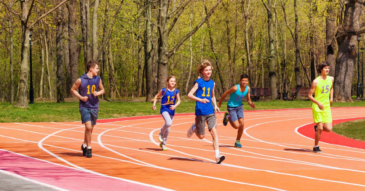 Long Term Athletic Development|Five young athletes running on an outdoor track surrounded by trees. They are wearing various blue and neon outfits