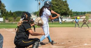 Newell Softball|A softball player in a white uniform is swinging at a pitch