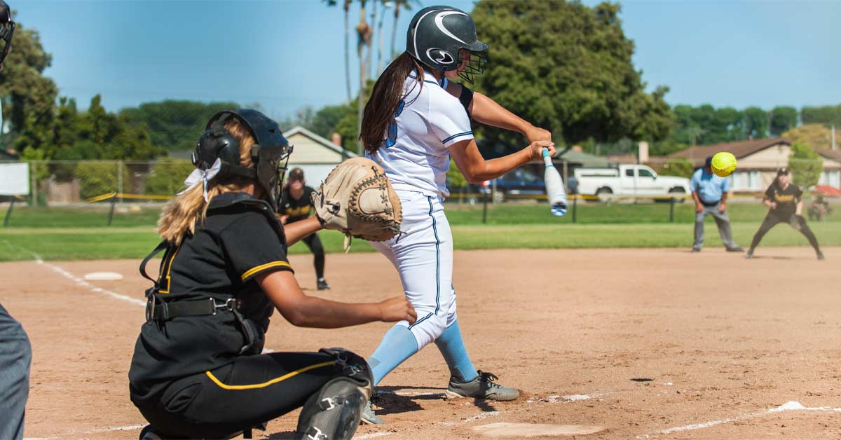 Newell Softball|A softball player in a white uniform is swinging at a pitch