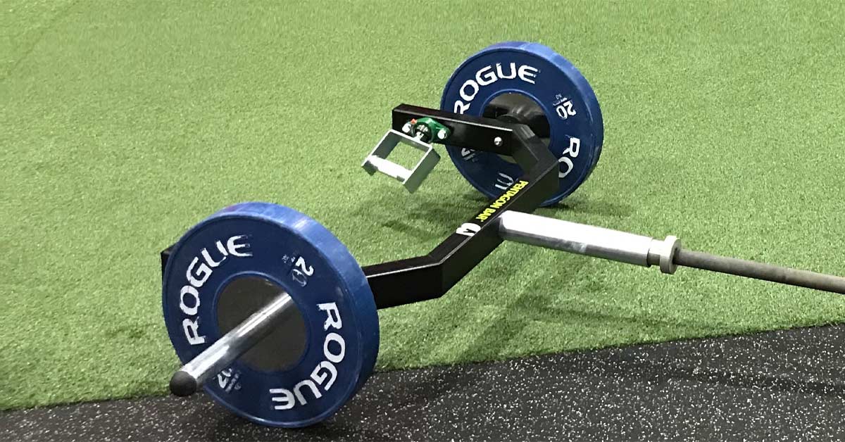 A black hex bar loaded with blue Rogue bumper plates is positioned on gym flooring
