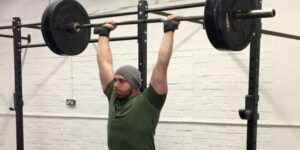 Overhead Press|Timeless Pressing|Overhead Press Periodization|A person lifting a barbell with weights in a gym