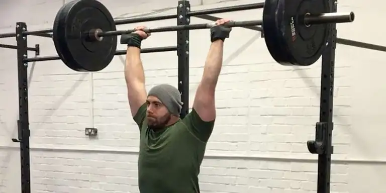 Overhead Press|Timeless Pressing|Overhead Press Periodization|A person lifting a barbell with weights in a gym