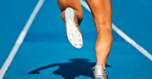 A runner with muscular legs is sprinting on a bright blue track