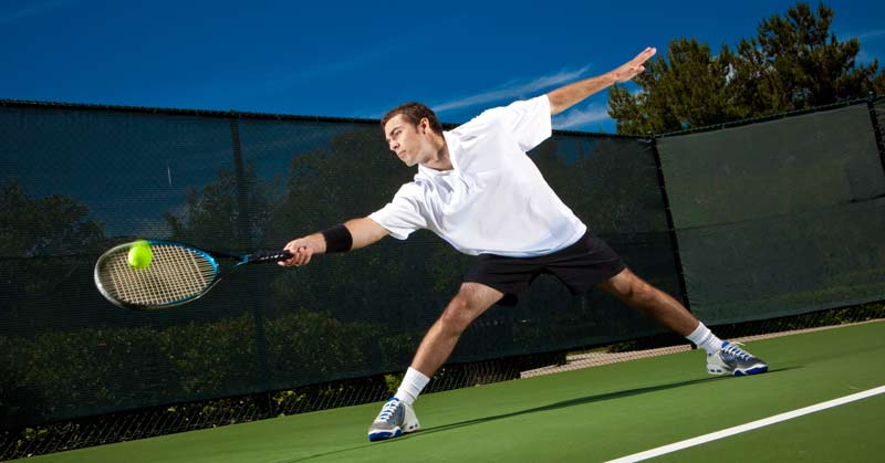 Tennis Agility|Soccer Cone Dribbling|Two men playing a fast-paced indoor sports drill on a green floor in a gym. One man dribbles a soccer ball past another. A woman in orange shorts and blue top observes from the background. Equipment and a poster appear on the walls.|Agility Video Sequence
