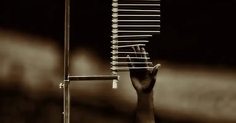 A monochrome image of a hand reaching up towards a set of horizontal rods attached to a vertical pole