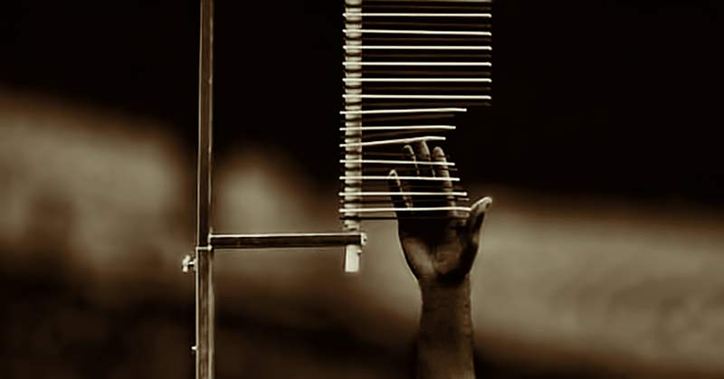 A monochrome image of a hand reaching up towards a set of horizontal rods attached to a vertical pole