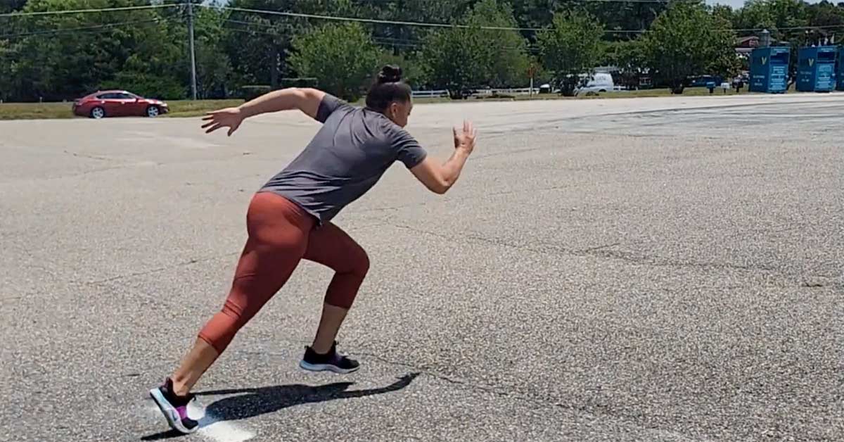 Volleyball Speed|A person wearing a black RISE T-shirt and gray leggings is sprinting on a grassy field. The image captures mid-motion