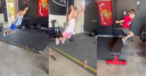 Three young children take turns jumping over a small hurdle indoors