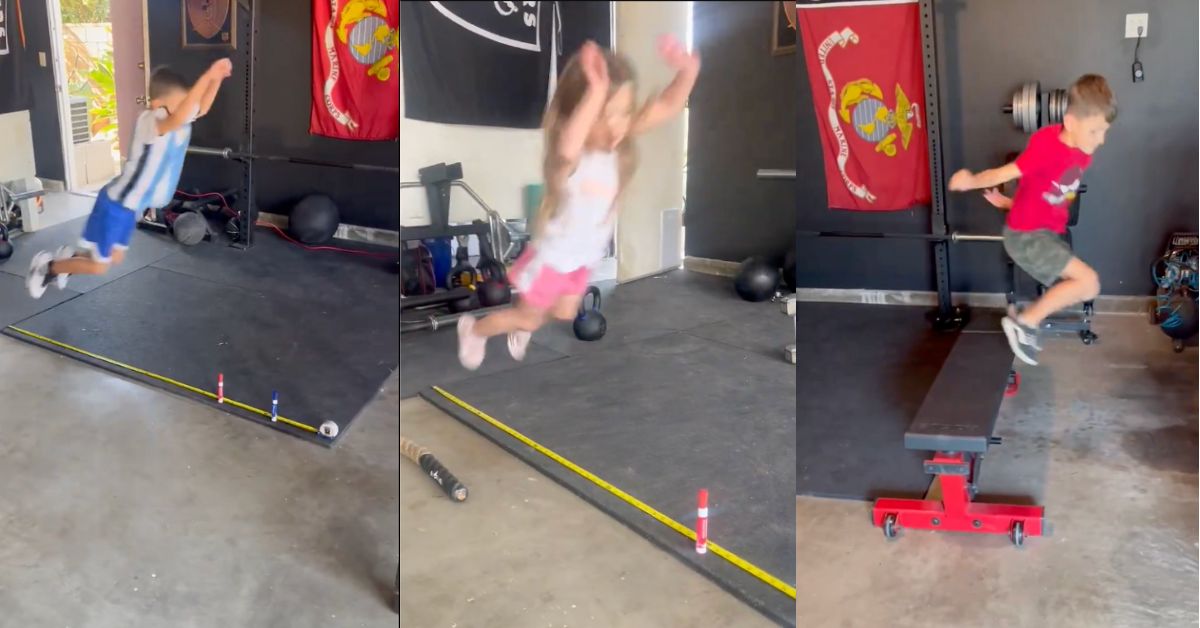 Three young children take turns jumping over a small hurdle indoors